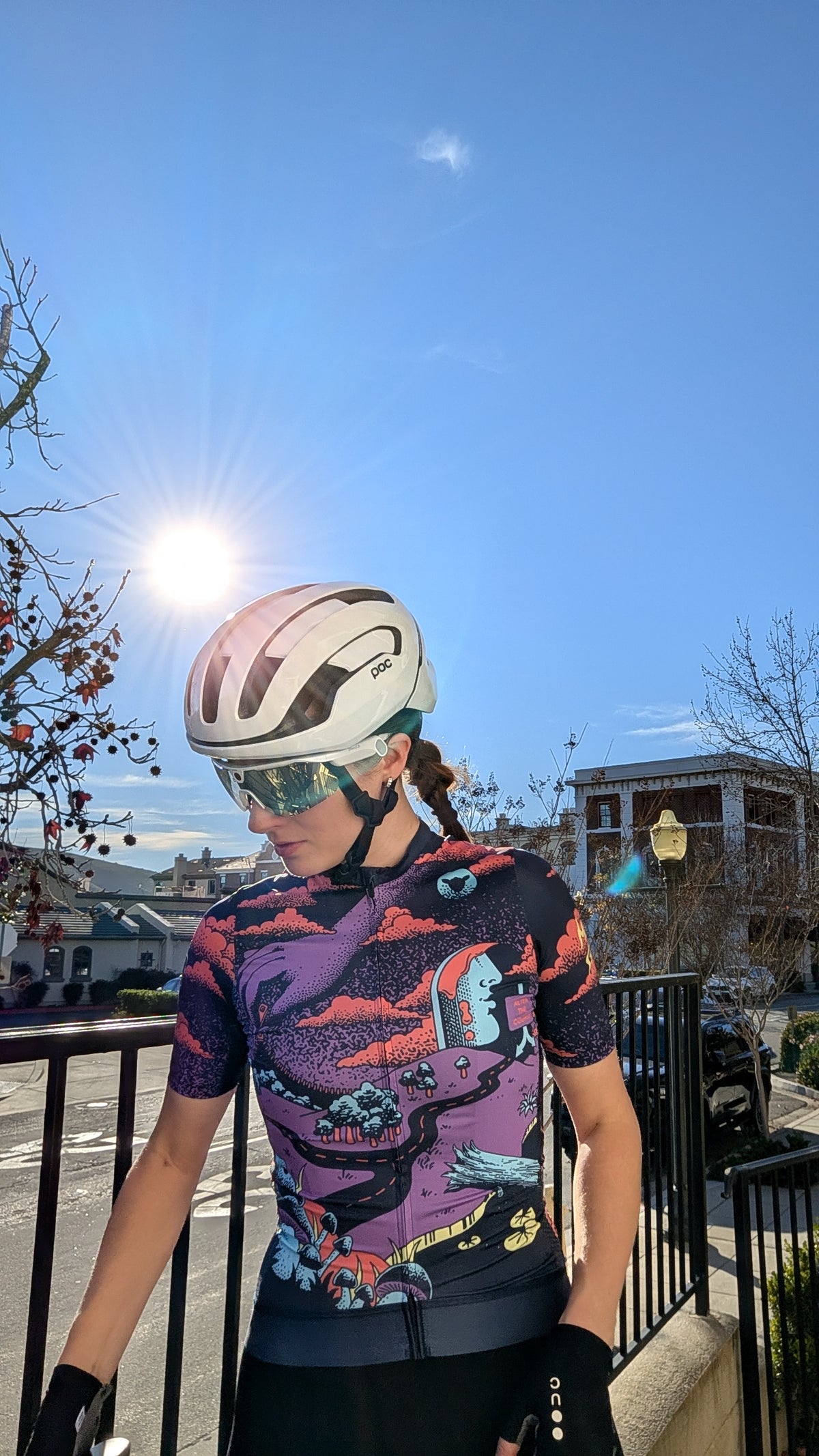 A woman is wearing a short-sleeve cycling jersey featuring an artistic, psychedelic-style print with purple